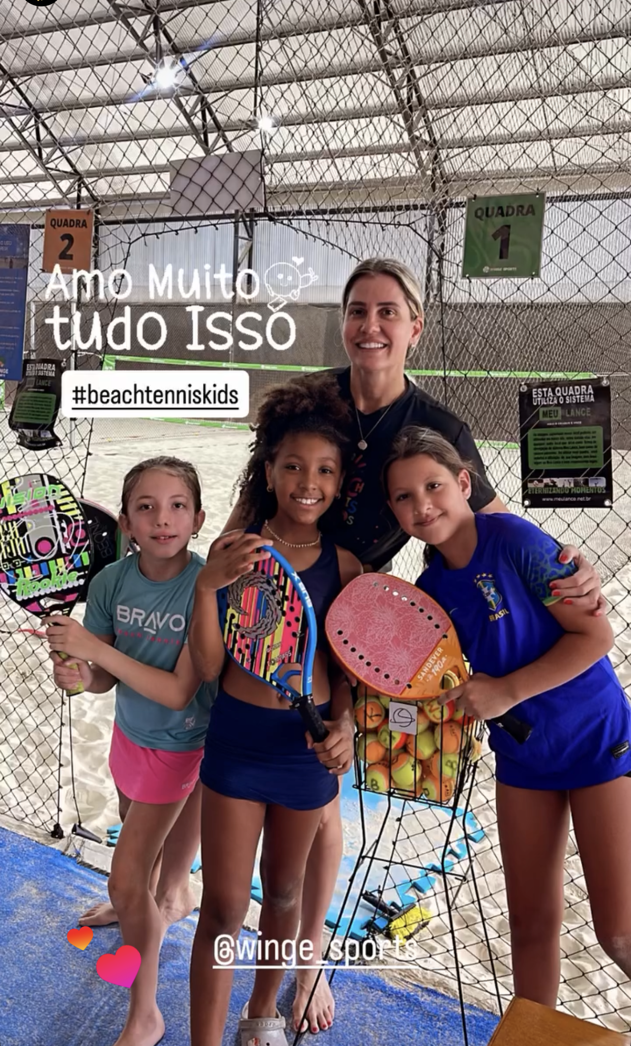 10 Benefícios Essenciais do Beach Tennis Kids: Saúde e Emoção em Quadra 2 Professora sorridente ao lado de três alunas de Beach Tennis Kids, com raquetes coloridas, em uma quadra de areia. A imagem transmite a alegria e o aprendizado em grupo.