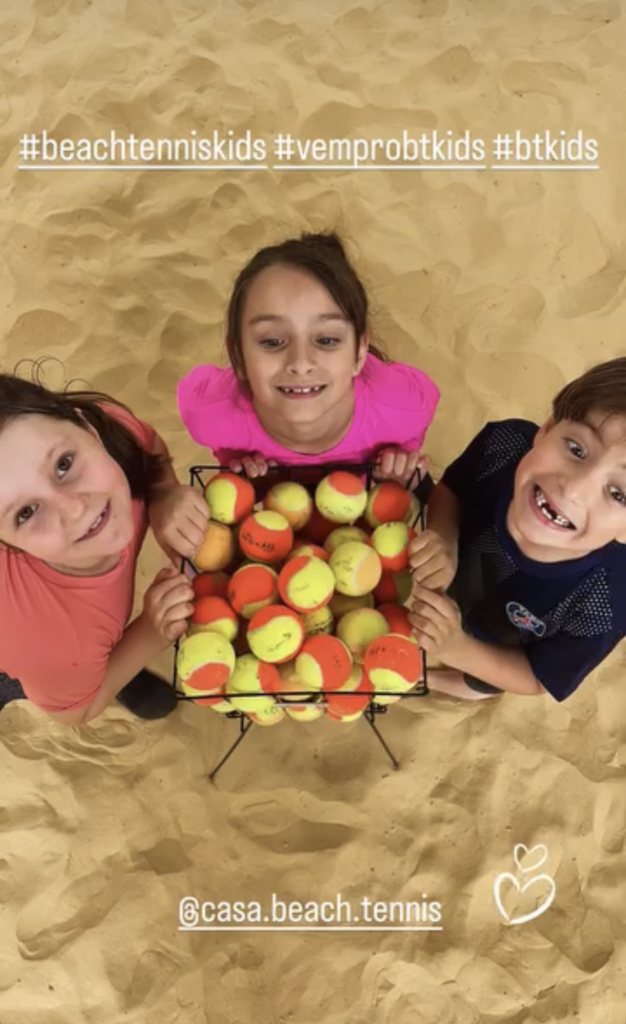 10 Benefícios Essenciais do Beach Tennis Kids: Saúde e Emoção em Quadra 36 Crianças sorridentes em torno do cesto de bolas, esperando a aula de Beach Tennis Kids começar.