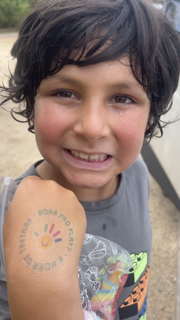 Criança, suada, sorrindo mostrando a mão com a tatuagem da Beach Tennis Kids.