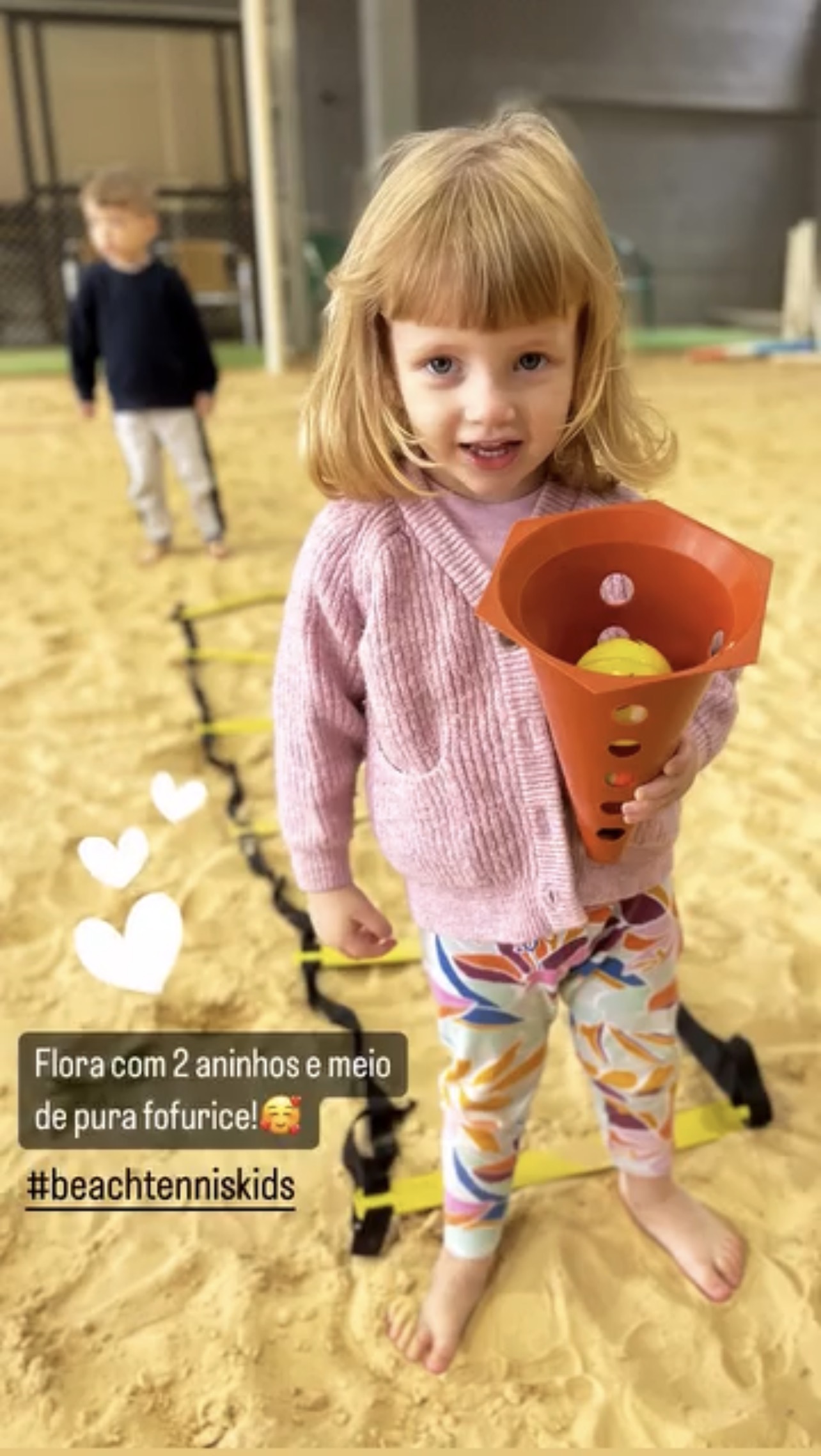 Qual a idade ideal para começar no Beach Tennis Infantil? 2 Aluna de 2 anos brincando com cone e bolinha de beach tennis na areia, demonstrando os primeiros contatos infantis com o esporte.